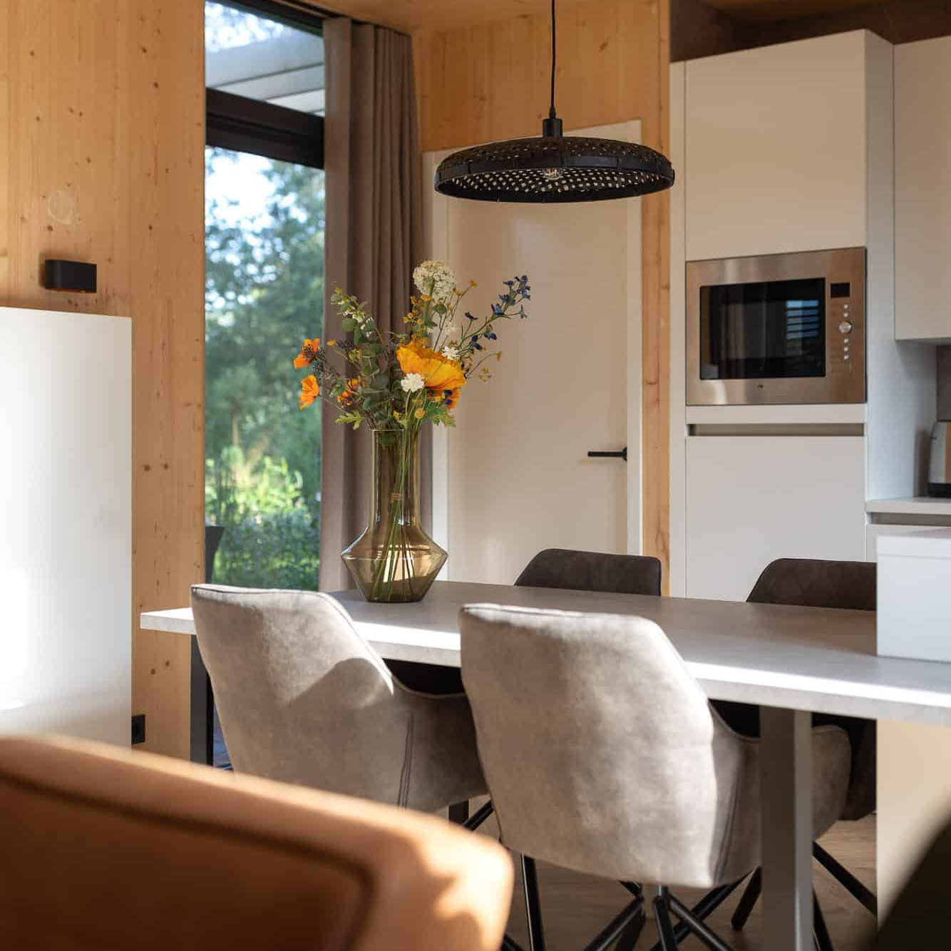 Moderne eetkamer met houten plafond, grijze stoelen en verse bloemen in Panorama lodge Markelo