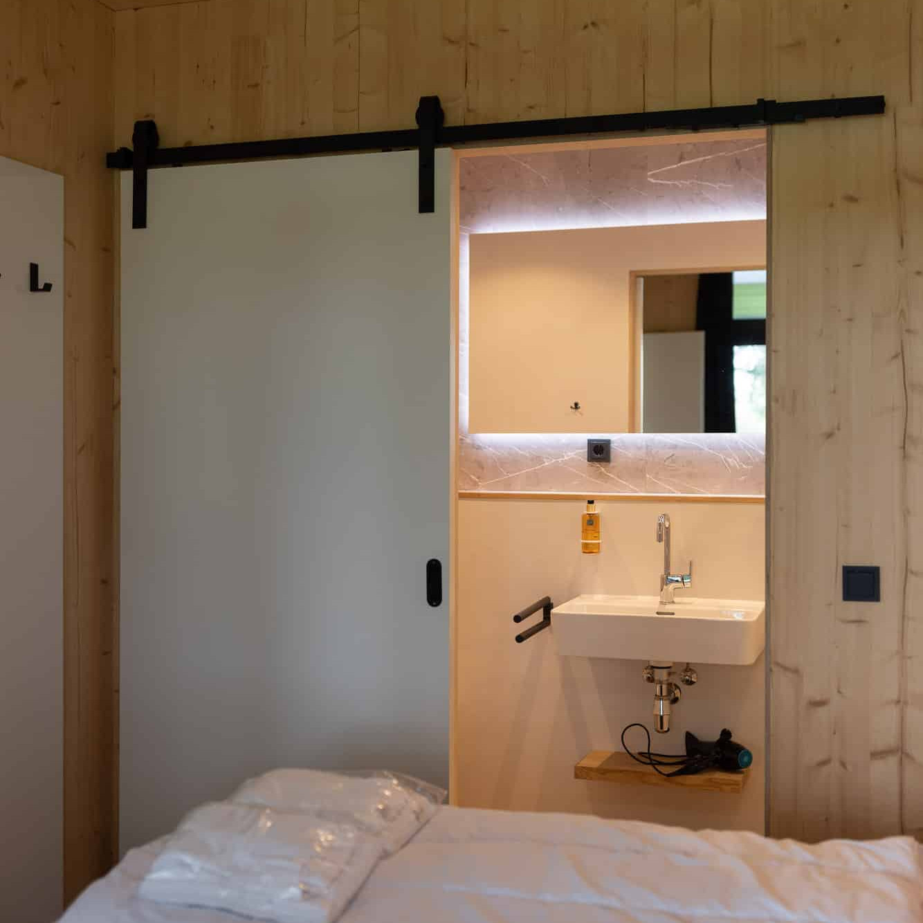 Slaapkamer met houten wanden en schuifdeur naar badkamer met verlichte spiegel in Panorama lodge Markelo