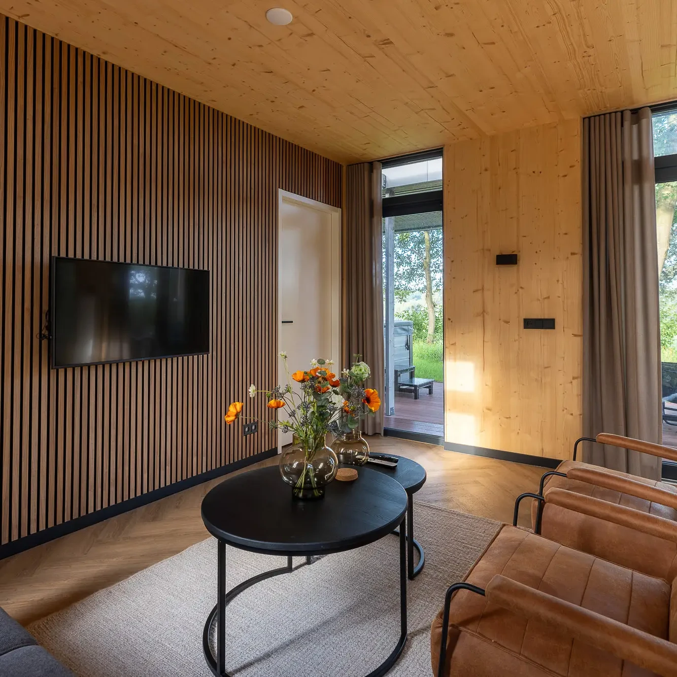 Luxe woonkamer met houten lamellenwand, flatscreen TV en uitzicht op natuur in Panorama lodge Markelo