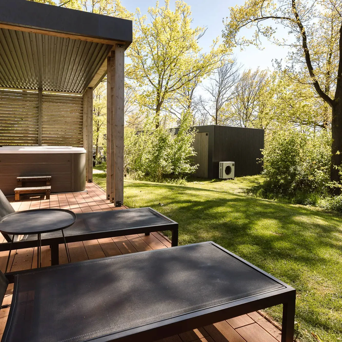 Ligbedden en jacuzzi op houten terras van luxe Panorama lodge in Markelo met uitzicht op groene tuin