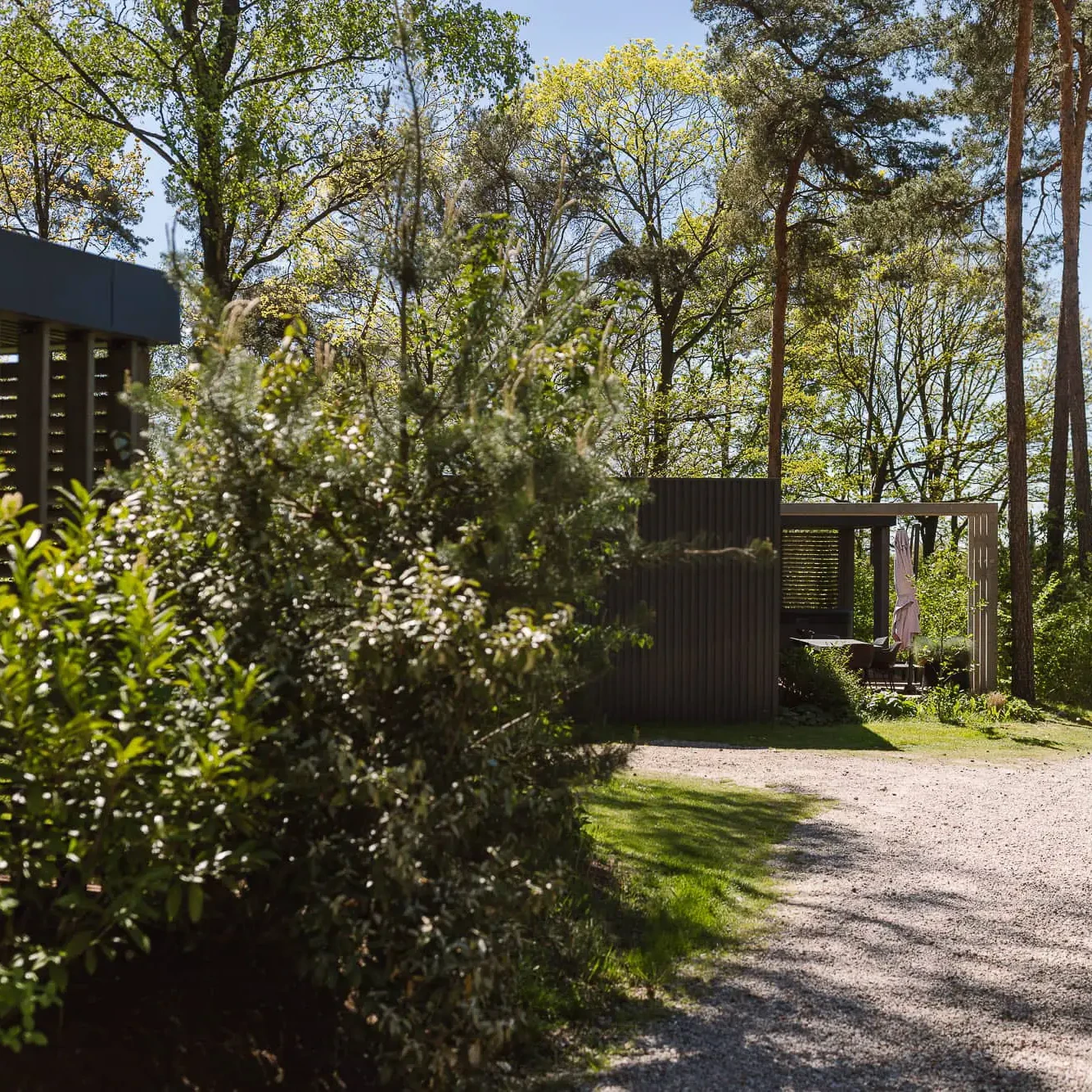 Grindpad tussen groene struiken naar moderne luxe lodges in bosrijke omgeving Markelo